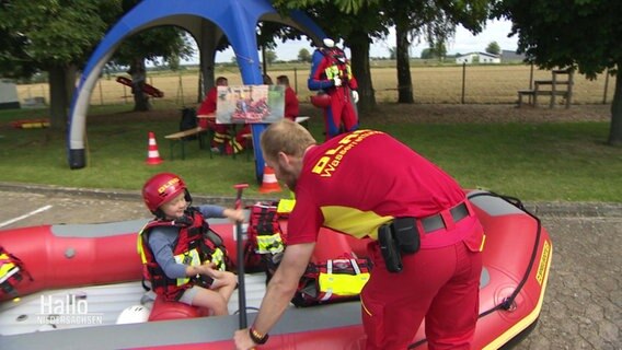 Ein Mann vom DLRG hilft einem kleinen Jungen in ein Schlauchboot. © Screenshot 