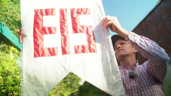 Ein Mann hängt eine Fahne mit der Aufschrift "Eis" auf. © Screenshot 