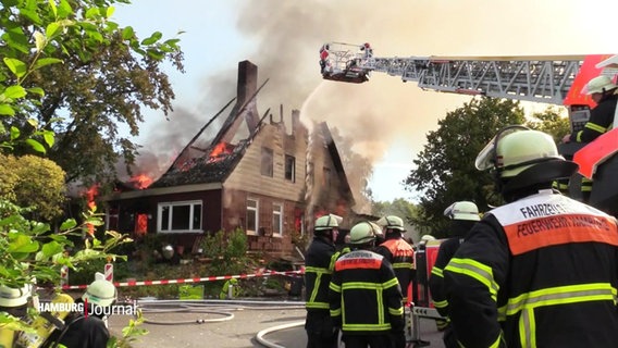 Blick auf ein brennendes Haus, dessen Dach bereits eingestürzt ist. Flammen und Qualm steigen empor. Feuerwehrleute versuchen auf einem Feuerwehrkran das Feuer von oben zu löschen. © Screenshot 