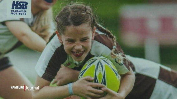 Ein Kampagnenbild zeigt ein lachendes Mädchen mit einen Rugby-Ball im Arm. © Screenshot 