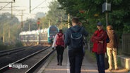 Menschen gehen am Bahnsteig vom Bahnhof in Bargteheide. Im Hintergrund sieht man einen türkisen Expresszug, der ohne Halt durchgefahren ist. © Screenshot 