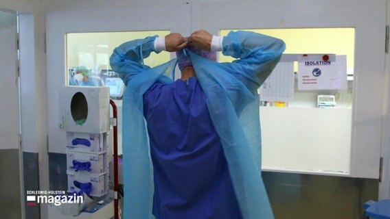 Ein Arzt zieht sich Schutzkleidung an. © Screenshot 
