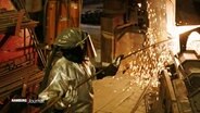 Ein Metallarbeiter steht in einer Industrieanlage. © Screenshot 