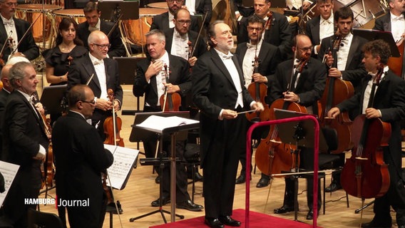 Ein Orchester mit Dirigent steht in einem Konzertsaal. © Screenshot 