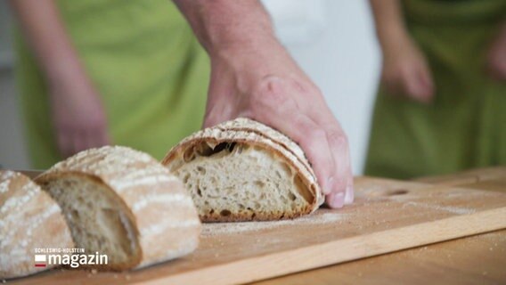 Jemand schneidet ein Brot auf einem Brettchen auf. © Screenshot 