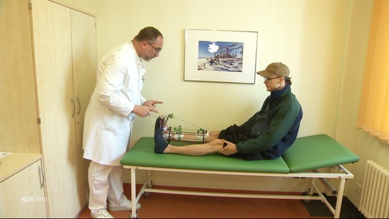 Ein am Bein verwundeter Mann wird von einem Arzt behandelt. © Screenshot 
