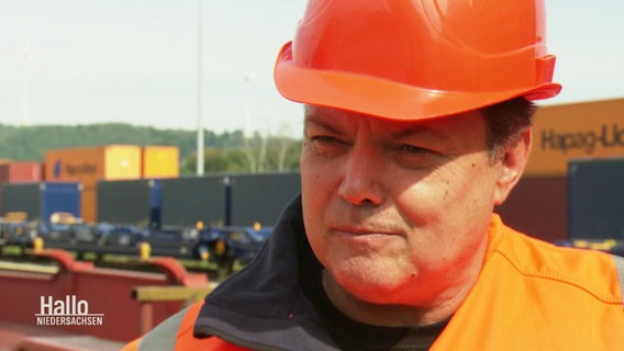 Ein Mann in Warnjacke und Helm in der Farbe Orange. © Screenshot 