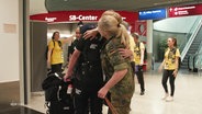Eine blonde Frau in Uniform umarmt eine Person am Flughafen. © Screenshot 