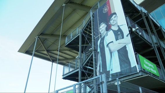 Plakat mit zwei Nationalspielern an der Wand eines Fussballstadions. © Screenshot 