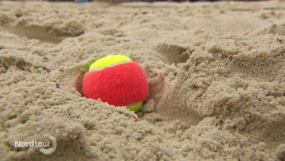 Ein Tennisball liegt im feinen Sand. © Screenshot 