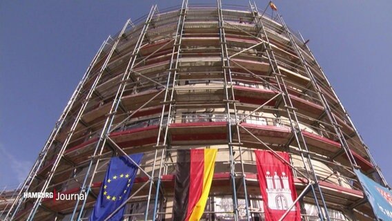 Eine Baustelle eines runden Gebäudes, an dem die europäische, deutsche und Hamburger Flagge hängen. © Screenshot 