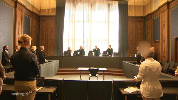 Ein Gerichtssaal, in dem mehrere Menschen stehen und Roben tragen. © Screenshot 