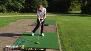 Eine Frau beim Abschlaf auf dem Golfplatz. © Screenshot 