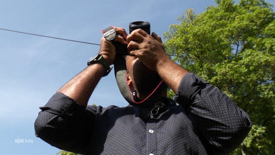 Ein Mann hält sich zum Fotografieren eine Kamera vor das Gesicht. © Screenshot 
