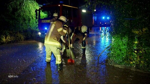 Einsatzkräfte der Feuerwehr auf einer Straße mit Schaufeln vor einem Einsatzfahrzeug. © Screenshot 