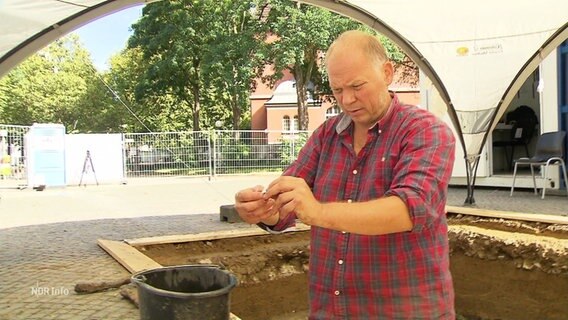 Archäeloge untersucht Fundstück auf einer Baustelle. © Screenshot 
