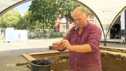 Archäeloge untersucht Fundstück auf einer Baustelle. © Screenshot 
