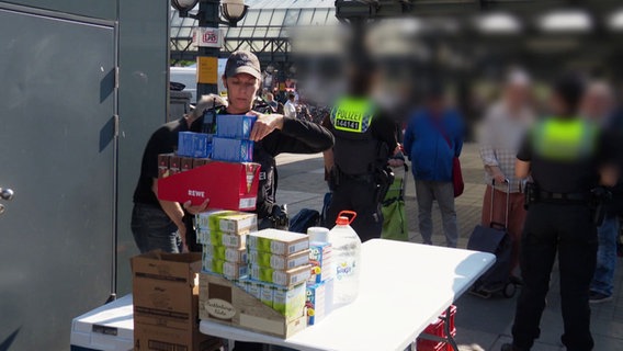 Ein Polizistin trägt aufgestapelte Lebensmittelverpackungen. © Screenshot 