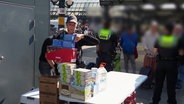 Ein Polizistin trägt aufgestapelte Lebensmittelverpackungen. © Screenshot 