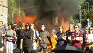 Demonstrierende stehen vor einem Feuer. © Screenshot 