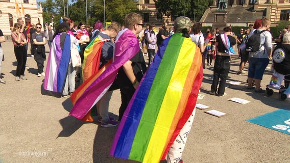 Menschen auf einer Demo tragen Flaggen verchiedener sexuellen und geschlechtlicher Identitäten als Umhänge. © Screenshot 