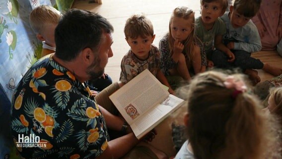 Ein Mann liest Kindern aus einem Buch vor. © Screenshot 