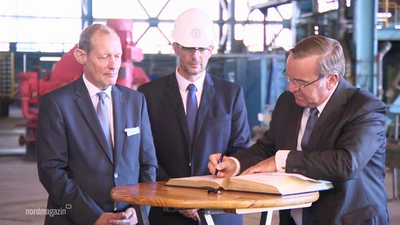 Pistorius und zwei Perosnen neben ihm mit Helmen. Er unterschreibt etwas. © Screenshot 