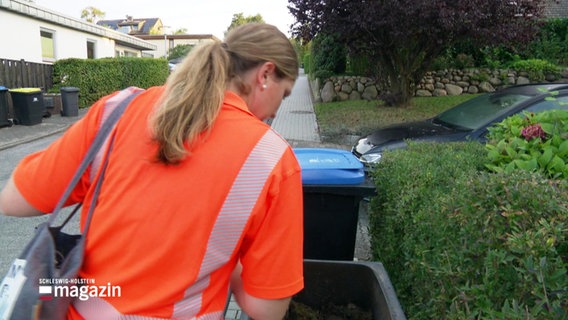 Eine Frau in orangefarbener Arbeitskleidung schaut in eine braune Biomülltonne. © Screenshot 