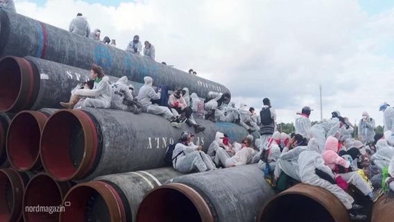 Demonstrierende sitzen auf großen Pipeline-Rohren. © Screenshot 