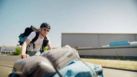 Eine Person transportiert mit einem Lastenfahrrad Säcke. © Screenshot 