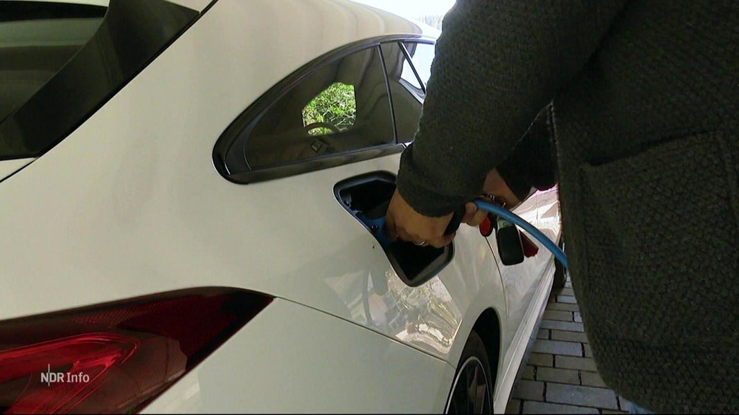 Eine Person schließt ein Ladekabel an sein Auto.