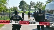 Polizisten und Einsatzfahrzeuge hinter einer Polizeiabsperrung. © Screenshot 