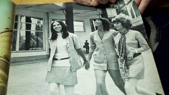 EIn zweiseitig abgedrucktes Schwarz-Weiß-Bild in einer älteren Modezeitschrift: Drei weibliche Models gehen ausgelassen in modischer Kleidung über einen Gehweg. © Screenshot 