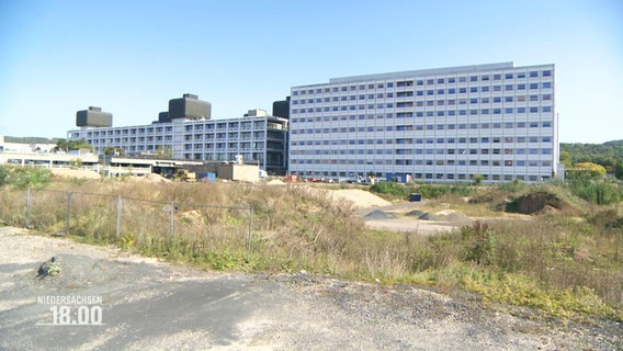 Blick auf ein brach liegendes, verwildertes Gelände vor einem größeren Klinik-Gebäude © Screenshot 