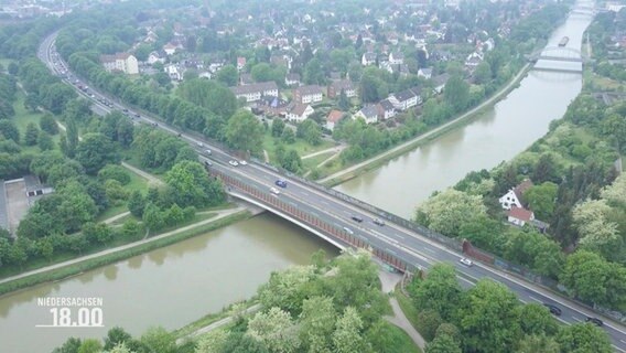 Blick aus der Vogelperspektive auf eine größere, mehrspurige STraße, die über eine breite Brück über einen Flusslauf nahe einer Kleinstadt führt. © Screenshot 