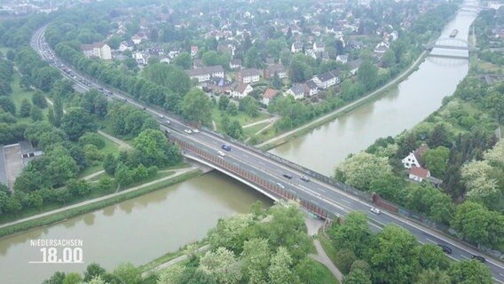 Blick aus der Vogelperspektive auf eine größere, mehrspurige STraße, die über eine breite Brück über einen Flusslauf nahe einer Kleinstadt führt. © Screenshot 