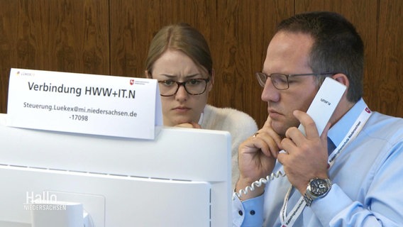 Eine Frau und ein Mann blick kritisch auf einen Computerbildschirm, der Mann hält einen Telefonhörer an sein Ohr. © Screenshot 