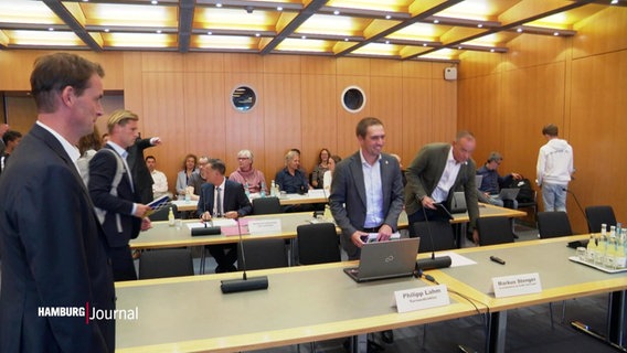 Menschen in einem Konferenzsaal. Viele tragen Anzüge und der Saal ist mit Holz ausgekleidet. © Screenshot 