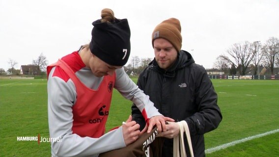 Jackson Irvine und eine weitere Person nebeneinander. Irvine signiert ein Trikot. © Screenshot 