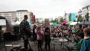 Menschen auf einer Bühne und ein Publikum davor unter freiem Himmel. © Screenshot 