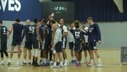 Eine Basketballmannschaft klatscht sich auf dem Feld in einer Sporthalle in der Mitte eines Kreises ab. © Screenshot 