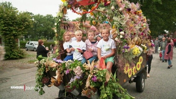Kinder sitzen auf einem mit bunten Blumen geschmückten Wagen. © Screenshot 