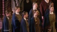 Ein lettischer Chor, gekleidet in traditionelle Gewänder, singt in einer Kirche. © Screenshot 