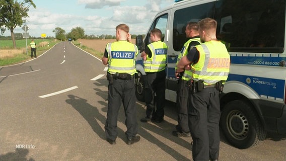 Beamte der Bundespolizei stehen an einer Landstraße neben ihrem Dienstfahrzeug. © Screenshot 