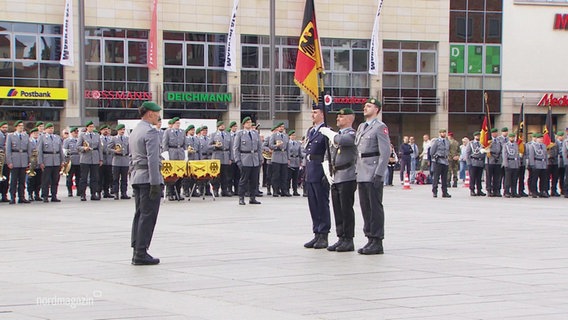 Soldaten in Uniform auf einem Platz mit Fahnen. © Screenshot 