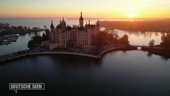 Das Schweriner Schloss liegt inmitten eines Sees, am Himmel ist ein Sonnenuntergang zu sehen. © Screenshot 