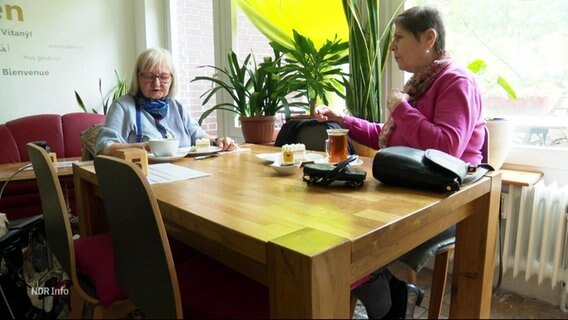 Zwei Frauen sitzen an einem Tisch und unterhalten sich. © Screenshot 