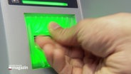 Eine Hand am Einzugschacht eines Geldautomaten. © Screenshot 