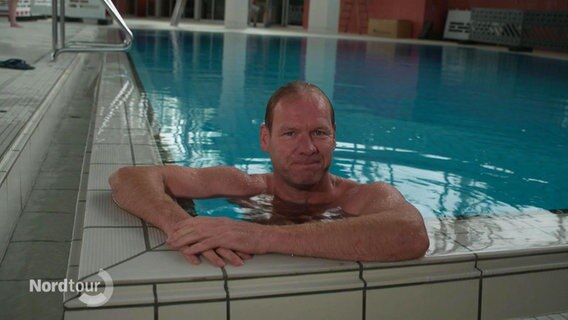 Thilo Tautz moderiert das "Nordmagazin" vom 07.10.2023 aus einem Schwimmbad. Er selbst ist im Becken, die Arme am Rand abgestützt. © Screenshot 