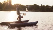 Ein fährt mit einem Wasserfahrrad, eine Art Spinning-Rad mit Luftkissen, über die Alster während des Sonnenuntergangs © Screenshot 